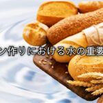 水の背景に並べられたパンと小麦の穂。パン作りにおける水の重要性を表すイメージ