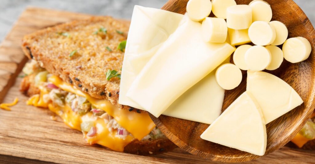 木製プレートに並べたスライスチーズと丸型プロセスチーズ、奥にチーズトースト